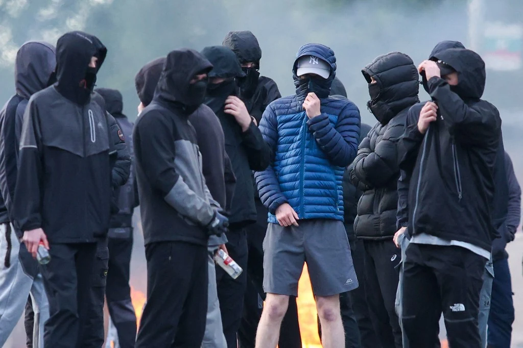 Manifestants masqués lors de violences anti-immigrés à Belfast, illustration d’un éditorial Afrology sur la montée de l’extrême droite en Europe